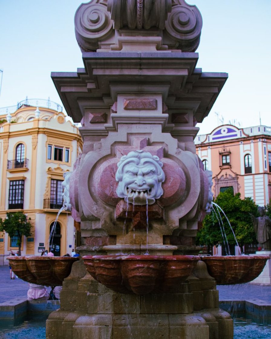 Fuente pública de piedra empotrada en un muro de Sevilla, con el agua cayendo en un pilón
