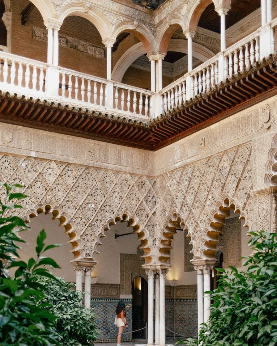 Patio de las Doncellas del Real Alcázar de Sevilla con la alberca central en calma y las arquerías de yesería mudéjar reflejadas en el agua, a primera hora