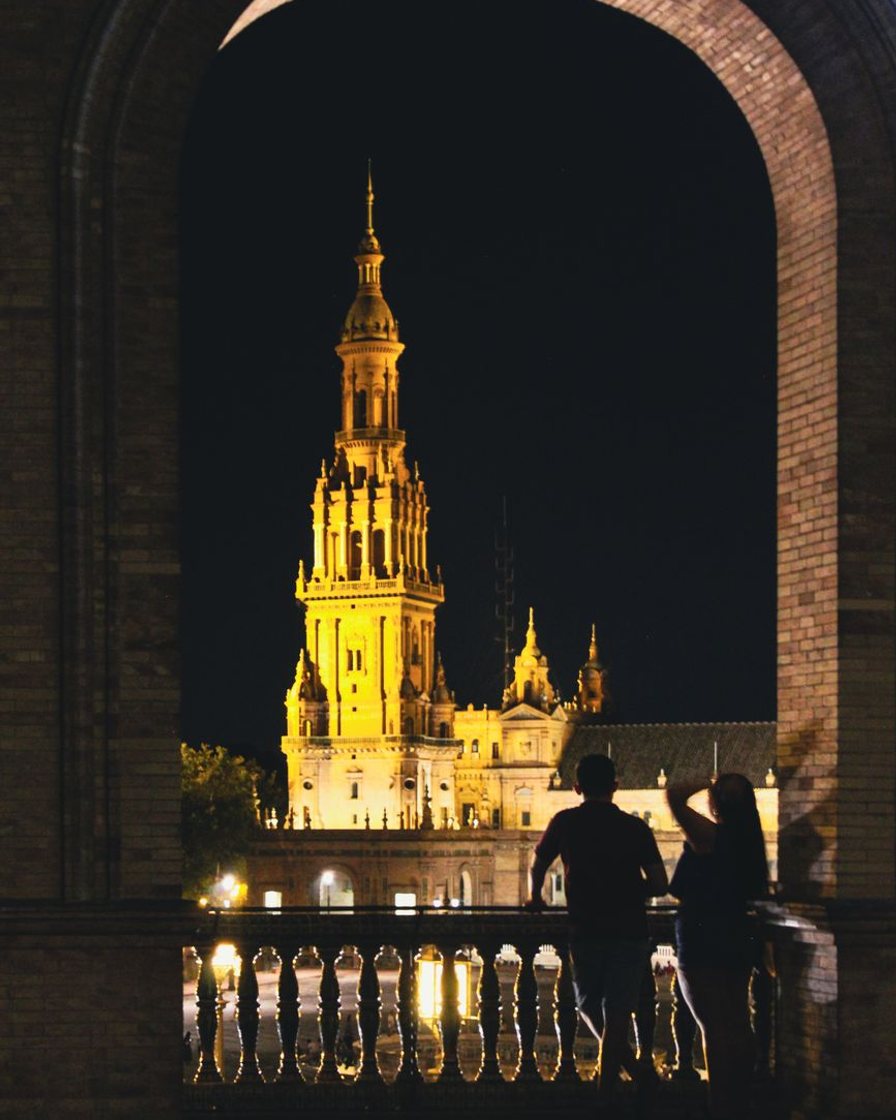 Fila de nazarenos con túnica morada y cirios encendidos entrando en la catedral de Sevilla por la puerta de San Miguel, al atardecer