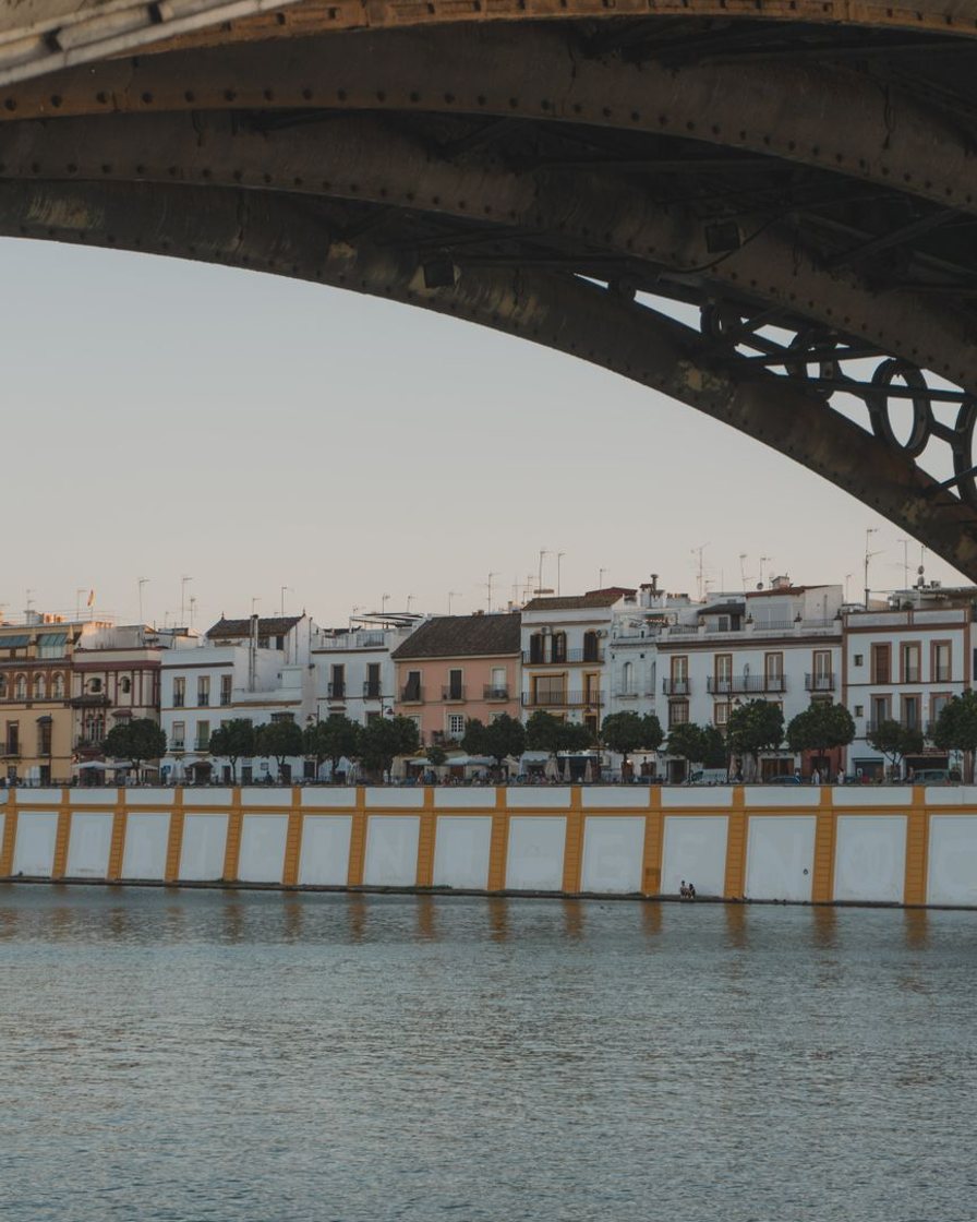 El puente de Isabel II de Sevilla de noche, iluminado, con gente cruzando a pie hacia Triana y la capilla del Carmen al fondo